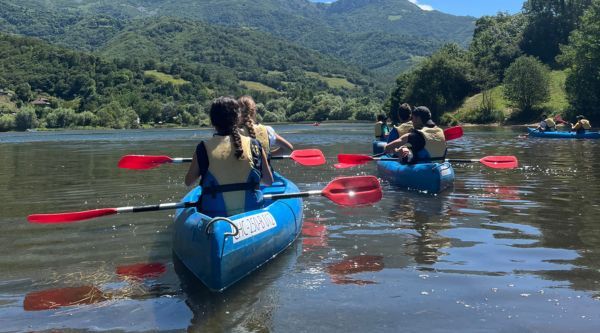 Piraguas remando en fila por un río entre colinas verdes