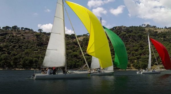 Veleros con spinnakers de colores navegando por el embalse en una regata por equipos