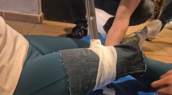 Manos vendando la pierna de un compañero en la posta de primeros auxilios de un raid de supervivencia